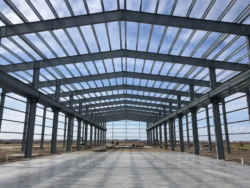 Interior de nave industrial en construcción con marcos de acero IPR y correas Monten visibles